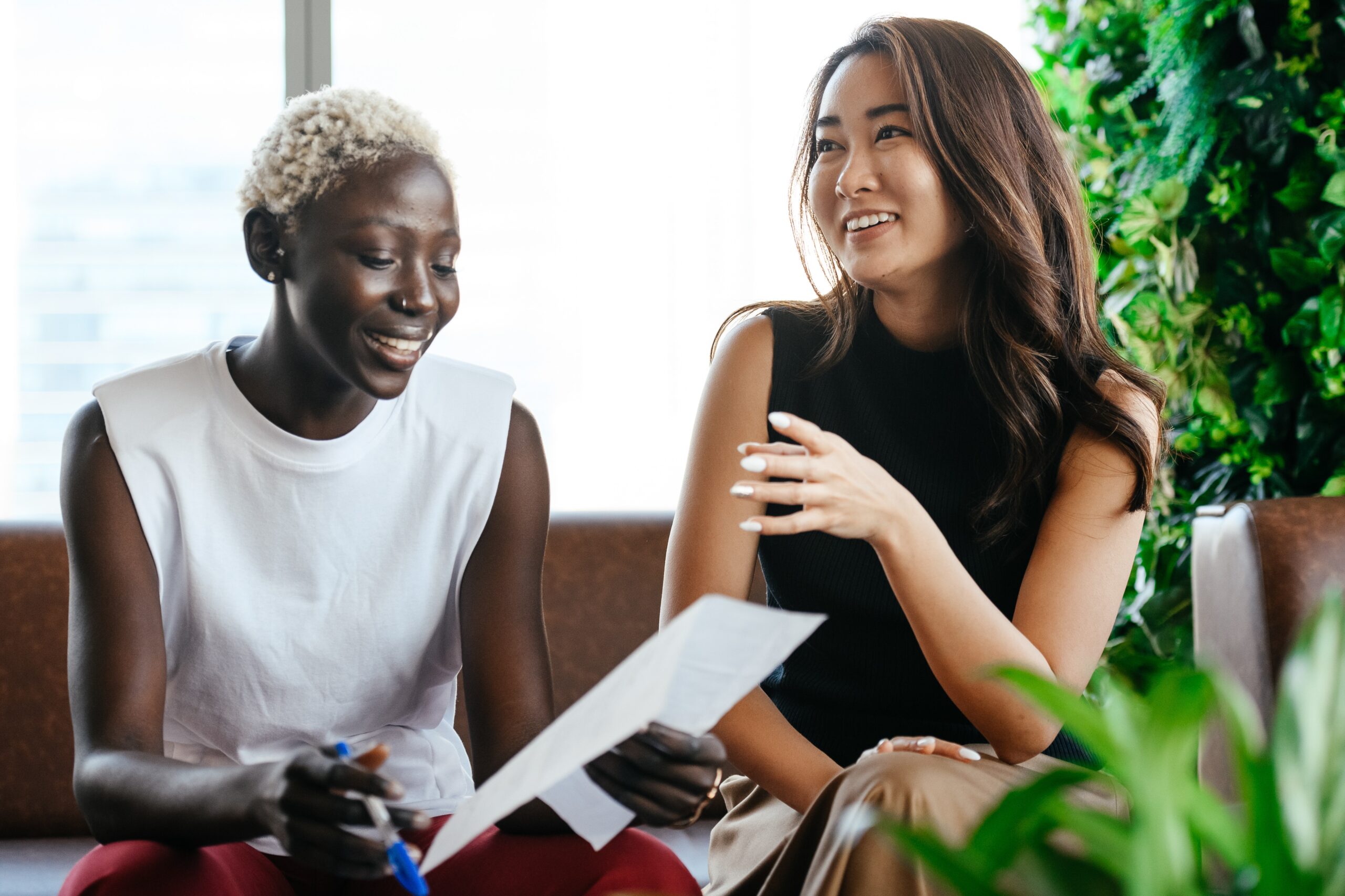 Two women professionals chatting on a couch in a co-working space. Blog post: 3 Overlooked principles for sustainable growth mindset".