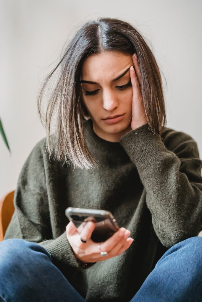 woman in a chair looking at her phone in her hand with a stressful and worried look on her face.