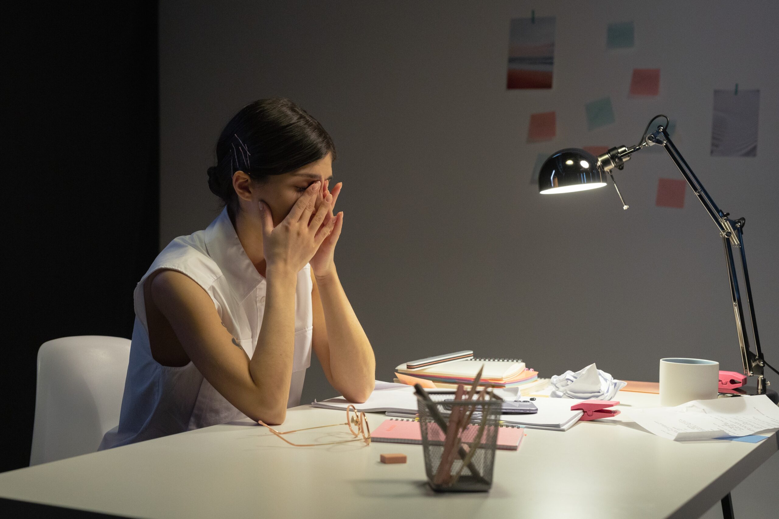 woman sitting at a disheveled desk with her hands over her face appearing stressed out.